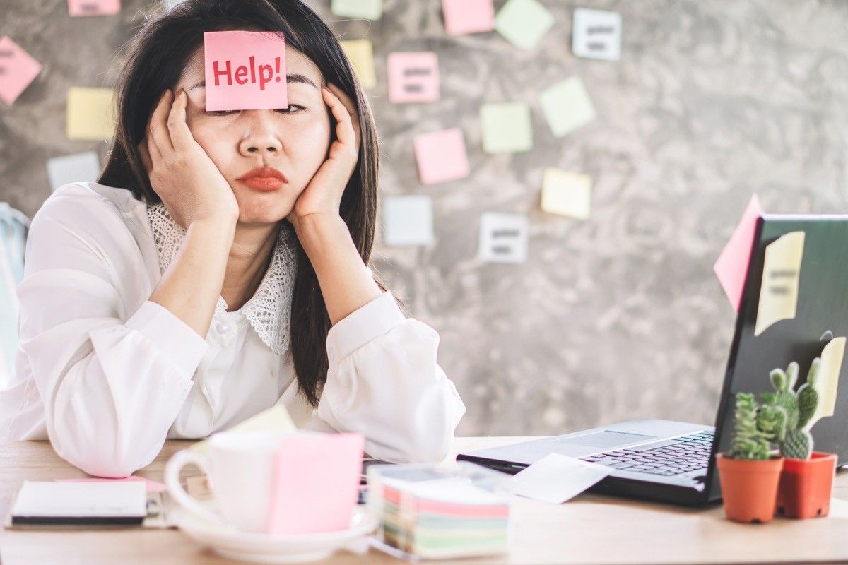 stressed Asian business woman tired from overworked sitting at office desk with note on face