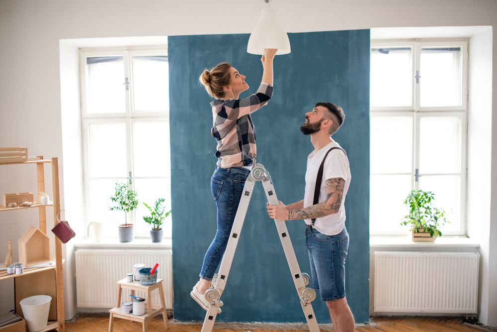 A young couple using a ladder to install a light in their home