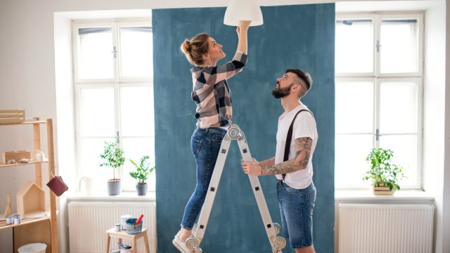 A young couple using a ladder to install a light in their home