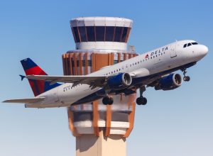 A Delta plane taking off with an air traffic control tower in the background