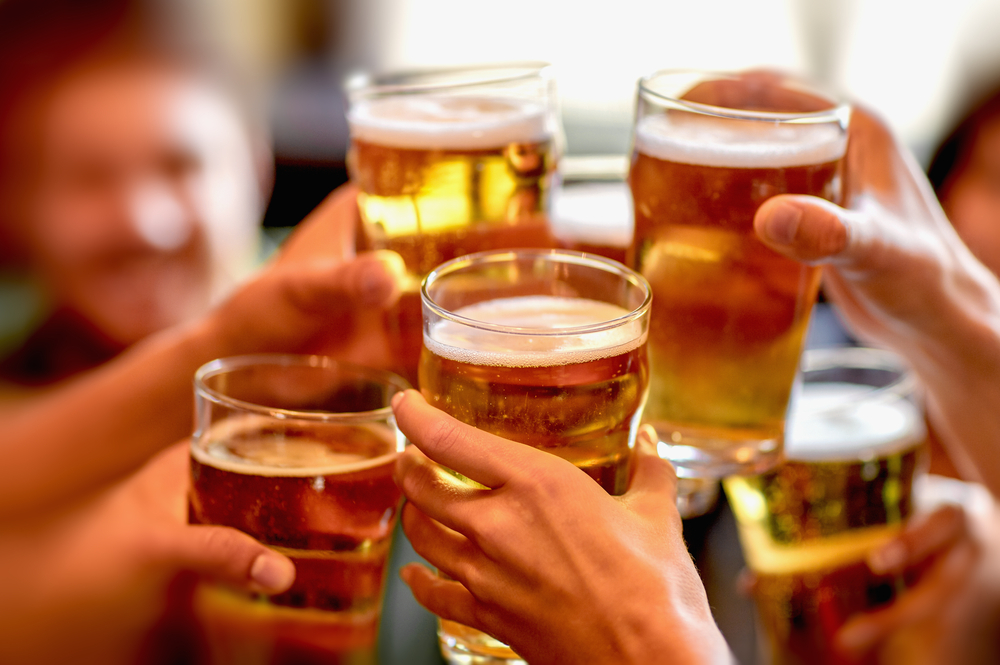 A closeup of a group of friends cheersing with pint glasses full of beer