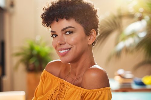 Portrait of natural beautiful girl smiling and looking at camera. Closeup face of brazilian young woman with curly hair. Charming african woman sitting at cafeteria.