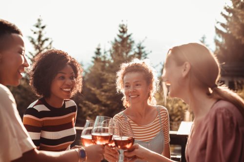 Nahaufnahme einer Gruppe von Freunden, die nach dem Abendessen auf der Terrasse im Wald Wein genießen