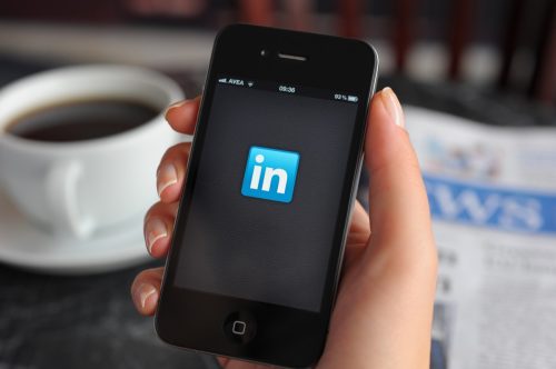 Woman hand holding an touching an Apple iPhone 4 in a coffee shop. iPhone 4 displaying start up screen of LinkedIn application. The iPhone 4 is a touchscreen slate smartphone and the fourth generation iPhone, developed by Apple Inc.