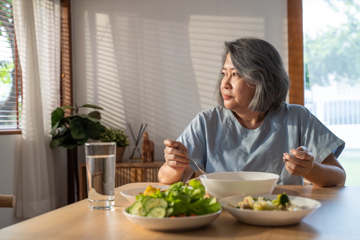 retired grandmother stay at home with painful face sitting alone on eating table in house.