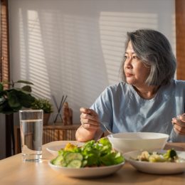 retired grandmother stay at home with painful face sitting alone on eating table in house.