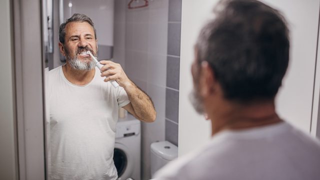 A middle-aged man looking in the mirror while brushing his teeth