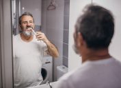 A middle-aged man looking in the mirror while brushing his teeth