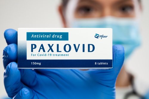 Uzice, SERBIA - Dec 22nd 2021: Medical worker holding medicine package box, Pfizer PAXLOVID antiviral drug,cure for Coronavirus infection,COVID-19 virus disease prevention and protection, illustration