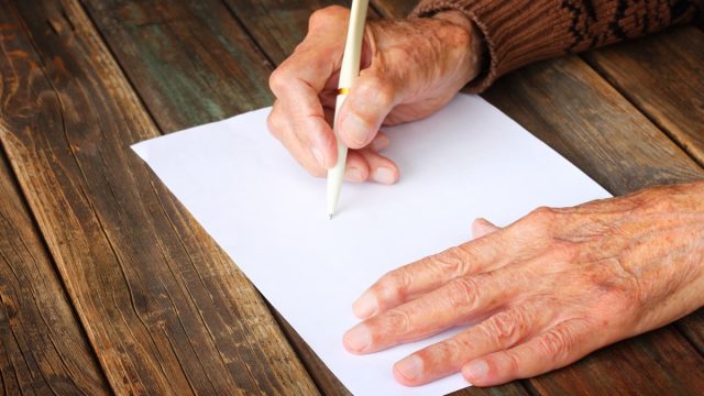 close up of elderly male hands on wooden table writing on blank paper
