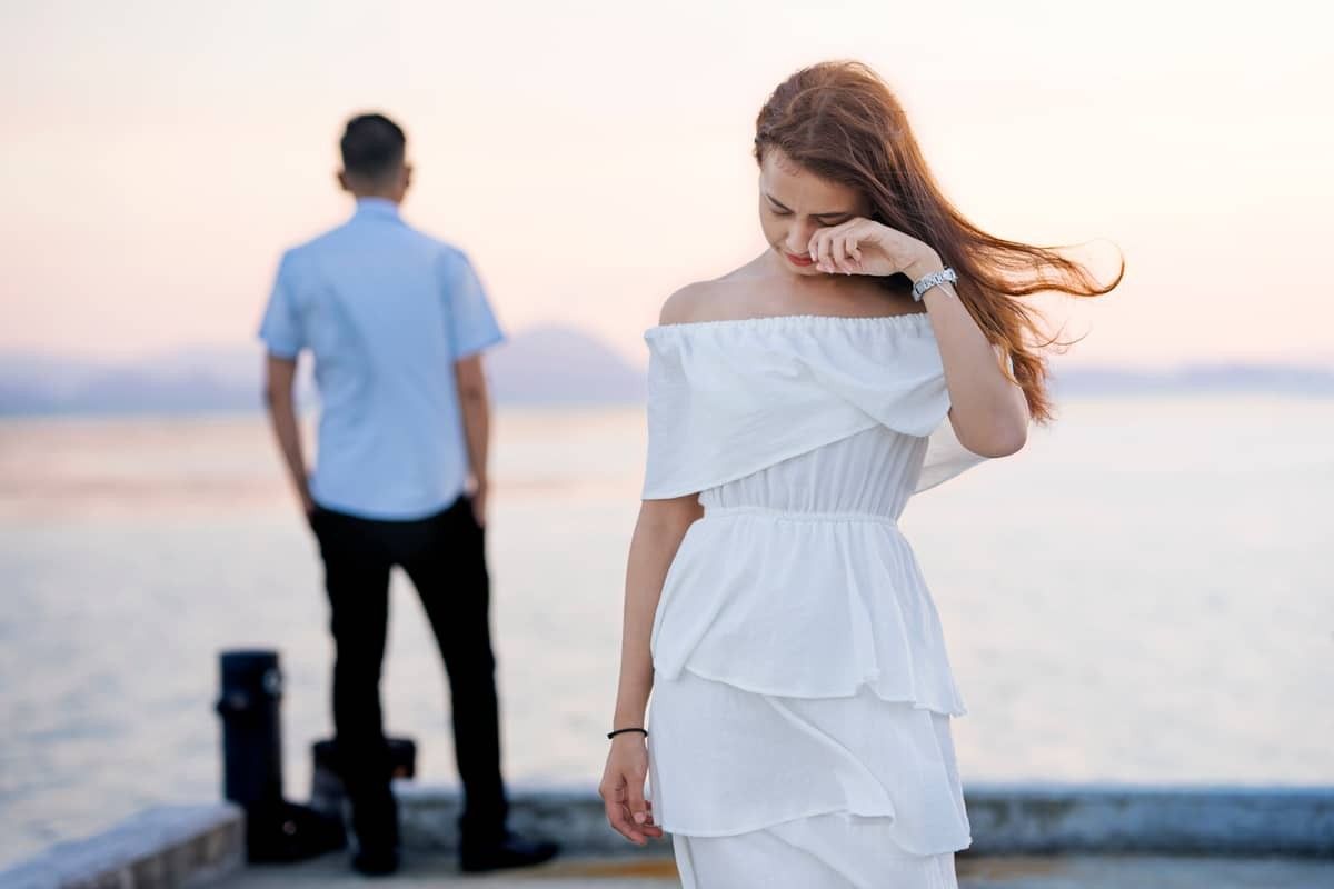 woman in white dress crying, man faces away from her in the background