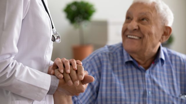 A senior male patient holding a doctor's hand in a checkup
