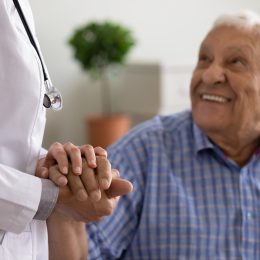A senior male patient holding a doctor's hand in a checkup