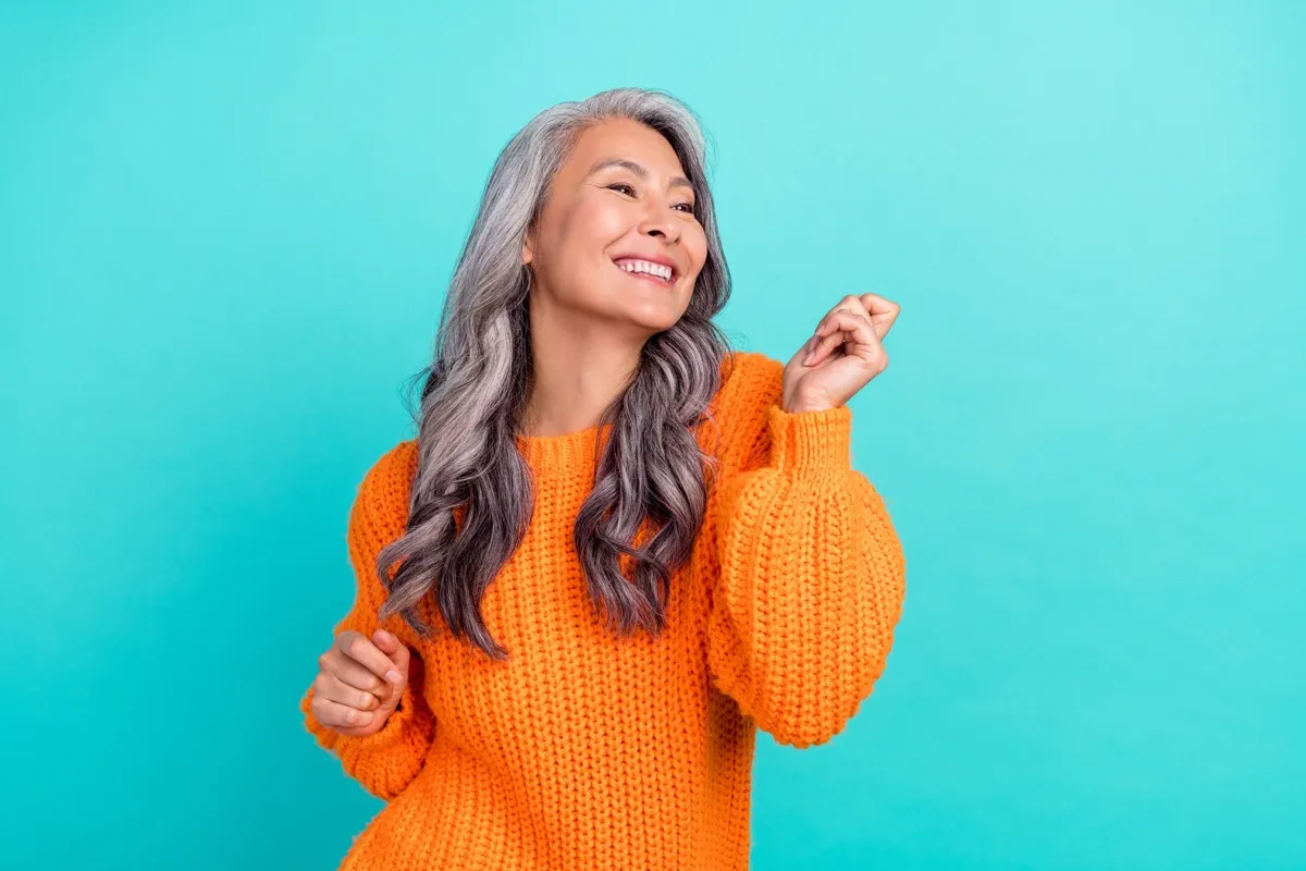 Woman in orange sweater with long wavy white hair