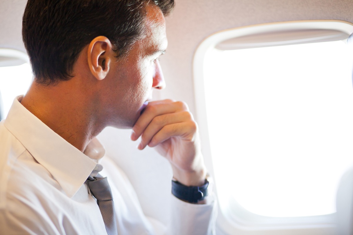 Un bărbat în gând se uită pe fereastra avionului