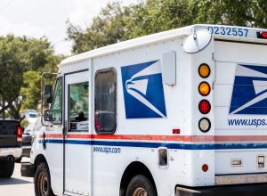 Small USPS van truck delivering packages in Florida, on street road driving