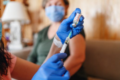 Un medic generalist vaccinează acasă un pacient în vârstă cu un spațiu de copiere.  Un medic face o injecție unei femei mari acasă.  O asistentă ține o seringă și folosește bumbac înainte de a face un vaccin Covid-19 sau coronavirus.