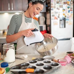 A woman using an electric mixer while baking cupcakes in her kitchen