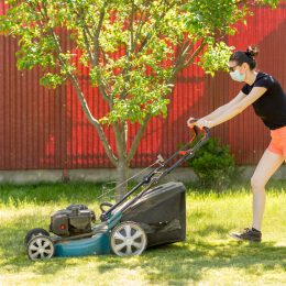 A woman mowing the lawn while wearing a face mask