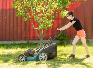A woman mowing the lawn while wearing a face mask