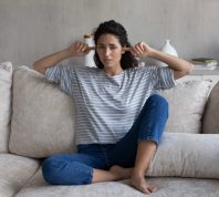 young woman sitting on sofa plugging her ears looking unhappy