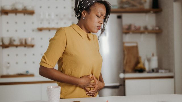 A young woman holding her stomach in pain while standing in the kitchen