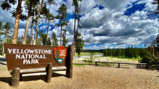 A sign for Yellowstone National Park with a scenic view behind it