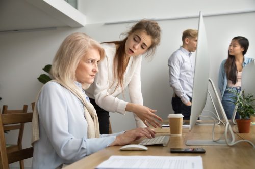 Young team leader correcting offended senior employee working on computer in office