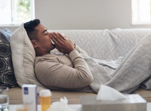 Shot of a young man blowing his nose while feeling sick at home