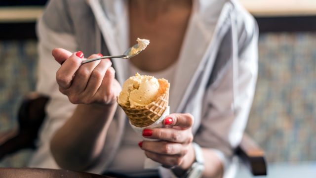 Girl holding spoon with ice cream cone, eating ice-cream in cafe, hands holding ice-cream