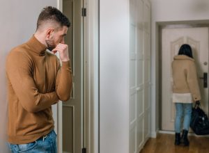 Young man watching sadly as his girlfriend walks out the door.