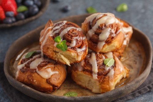 Homemade cinnamon buns in glaze on a dark plate with berries, dark background.