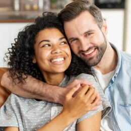 A couple sits on the couch embracing and smiling.