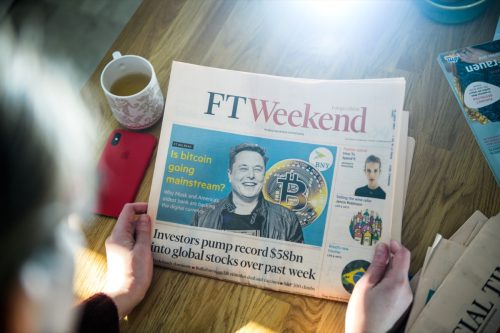 business woman reading Financial Times newspaper on kitchen counter with Elon Musk headline smiling and text Is bitcoin going mainstream.