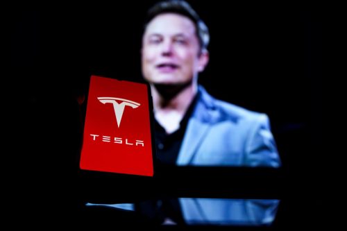 Tesla logo on screen and Elon Musk in a background.