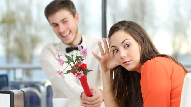 A young man shoving flowers at his date while she rolls her eyes.