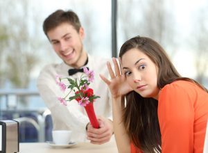 A young man shoving flowers at his date while she rolls her eyes.