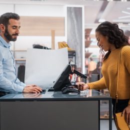 Young Woman at Counter Buys Clothes from Friendly Retail Sales Assistant,