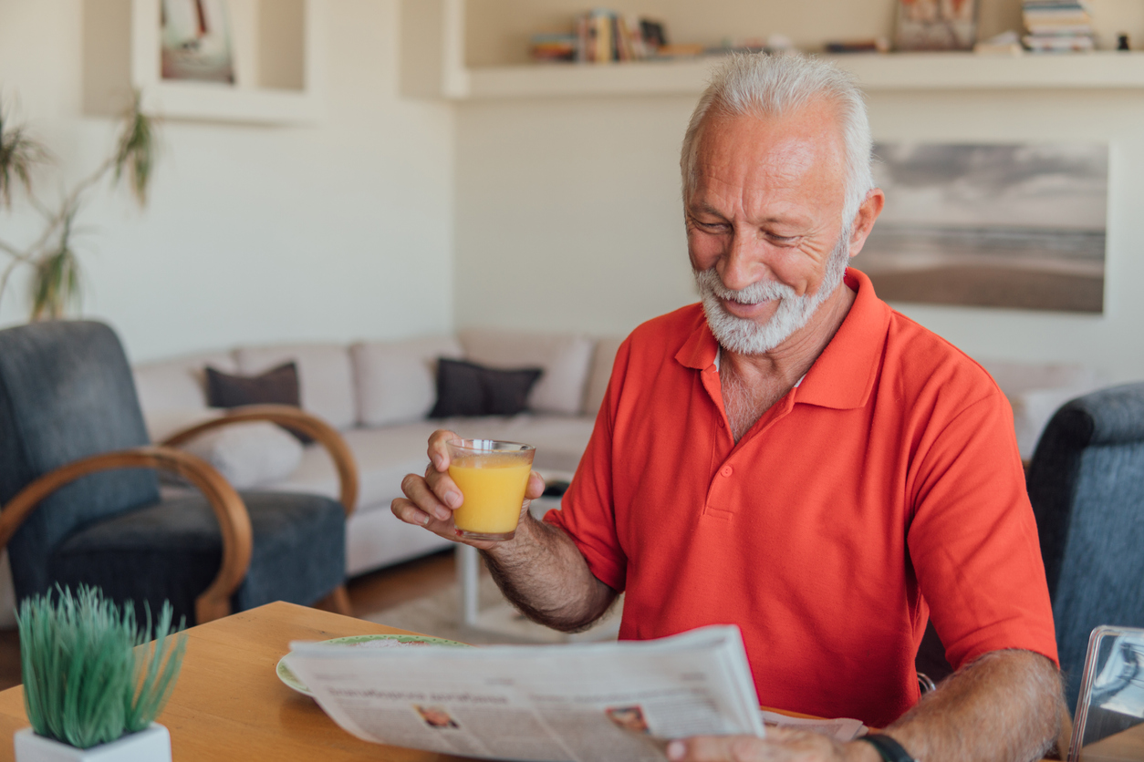 Възрастен мъж пие портокалов сок.