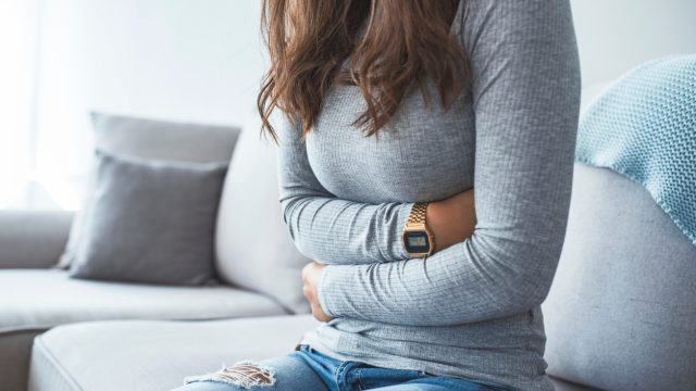 Woman sitting on a sofa holding her stomach.