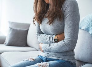 Woman sitting on a sofa holding her stomach.