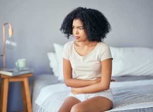Woman sitting on bed in discomfort.