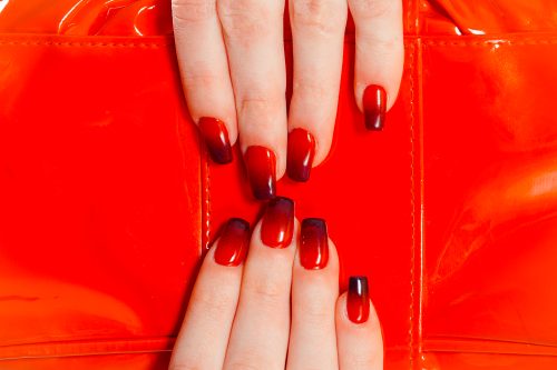 Nail Polish. Art Manicure. Modern style red black gradient Nail Polish. Stylish Colorful trendy Nails beauty hands isolated red bag as a background