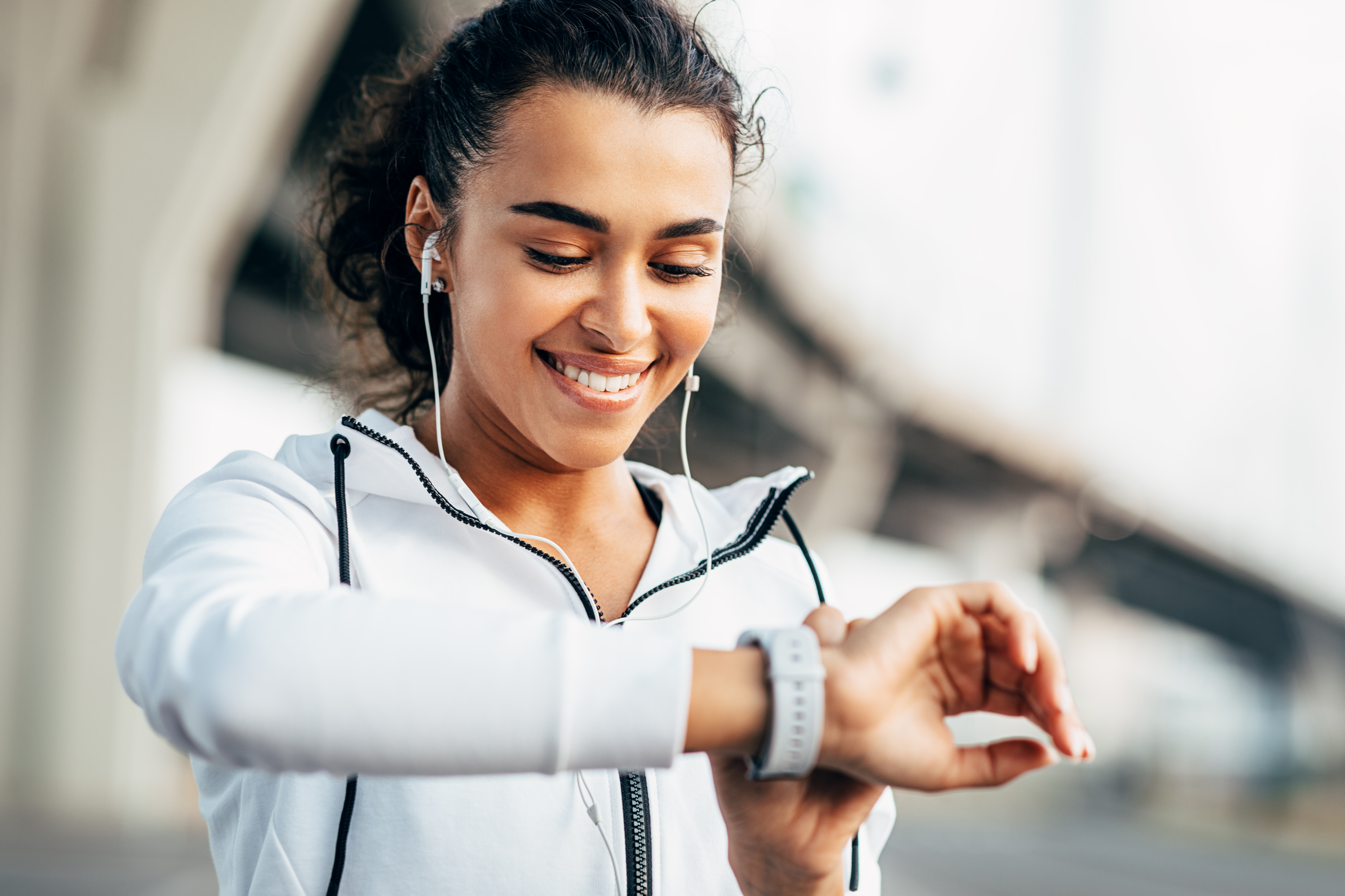 Mujer sonriente revisando su actividad física en un reloj inteligente. Atleta femenina joven mirando el rastreador de actividad durante el entrenamiento.