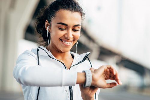 Người phụ nữ mỉm cười kiểm tra hoạt động thể chất của mình trên đồng hồ thông minh.  Nữ vận động viên trẻ nhìn vào máy theo dõi hoạt động trong quá trình tập luyện.