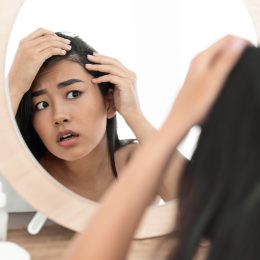 Worried woman looking at her hair in mirror.