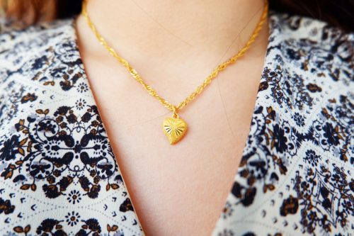 Pandantiv de aur și pandantiv de aur în formă de inimă pe gâtul unei femei asiatice.