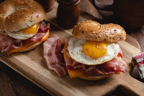 Breakfast bagel sandwich with fried egg, bacon and cheese on a wooden cutting board
