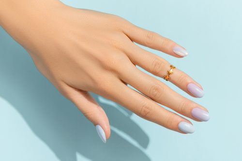 Bàn tay của phụ nữ với bộ móng tay hợp thời trang trên nền màu xanh.  Thiết kế móng tay mùa hè.  Ý tưởng thẩm mỹ viện