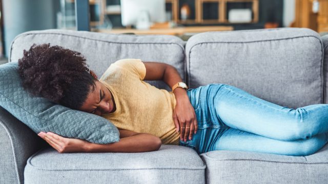 Woman lying on a couch with stomach discomfort.